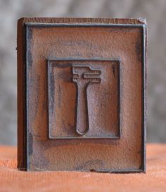 a square metal object with a hammer on it's side and the letter t in the middle