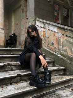 a woman sitting on the steps with her legs crossed and wearing black boots, in front of an old building