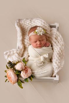 a newborn baby wrapped in a white blanket and surrounded by flowers is laying on a wooden crate