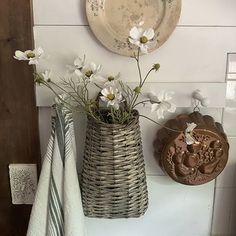 two vases with flowers in them sitting on a shelf next to a wall plaque