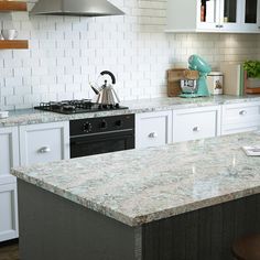 a kitchen with white cabinets and marble counter tops, an island in the middle has a tea kettle on it