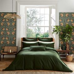 a bed with green sheets and pillows in a room next to a large potted plant