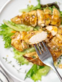 a white plate topped with chicken and lettuce next to a knife and fork