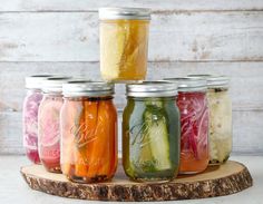 six mason jars filled with pickles, onions and cucumbers on a wooden board