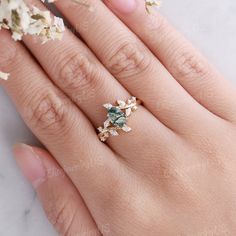 a woman's hand with a ring on it and some flowers in the background