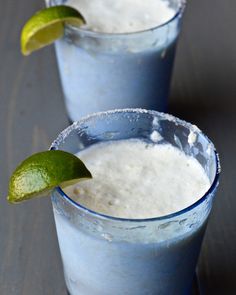 two glasses filled with blue custard and limeade on top of a wooden table