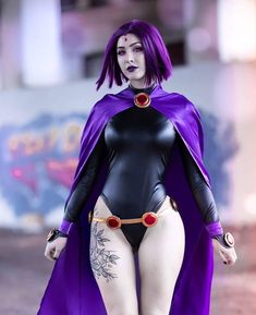 a woman in a purple cape and black bodysuit walking down the street with her hands on her hips