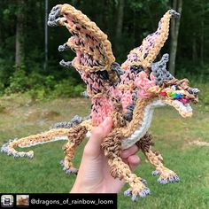 a hand holding up a crocheted dragon in the middle of a grassy area