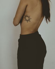 a woman with a sun tattoo on her back, standing in front of a white wall