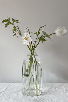 some white flowers are in a clear glass vase on a tableclothed surface,