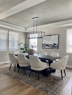 a dining room table with white chairs and a rug on the floor in front of it