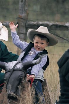 a young boy riding on the back of a horse next to an older man wearing a cowboy hat