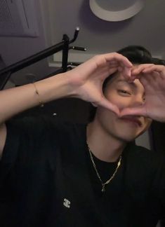 a person making a heart with their hands in front of the camera while wearing a black shirt