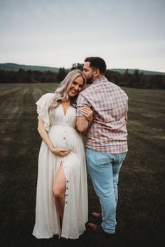 a pregnant woman in a white dress standing next to a man wearing a plaid shirt