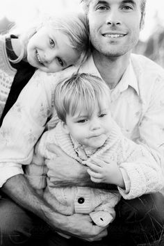 black and white photograph of a man with two children on his lap, smiling at the camera