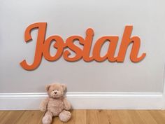 a teddy bear sitting in front of the name joshua on a wall with an orange background