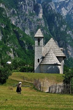 an old church on the side of a mountain with a woman walking in front of it