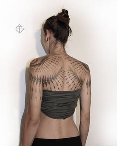 the back of a woman with tattoos on her upper and lower body, in front of a white wall