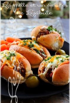 three hot dogs on buns with cheese and vegetables in the middle, sitting on a black plate