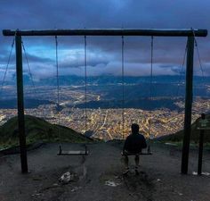 a man sitting on a swing at the top of a hill overlooking a cityscape