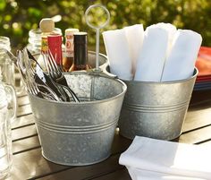 two metal buckets filled with utensils sitting on top of a wooden table