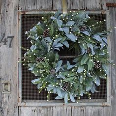 a wreath with pine cones and greenery is hanging on the side of a building