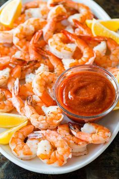 a plate with shrimp, lemon wedges and ketchup on it next to a bowl of dipping sauce