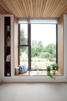 an empty window seat in front of a wooden shelf with books and plants on it