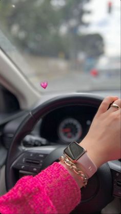 a woman driving a car with a pink bracelet on her wrist and an apple watch