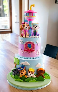 a three tiered cake decorated with cartoon characters on the front and sides, sitting on top of a wooden table