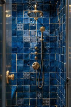 a blue tiled shower with gold fixtures and hand held shower head in the corner,