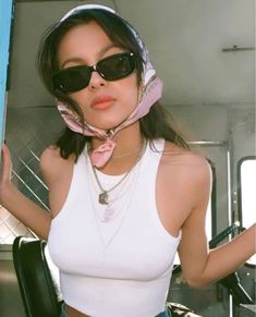 a woman wearing sunglasses and a pink scarf around her neck is posing for the camera