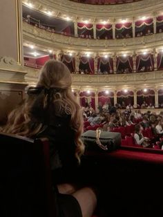 a woman is sitting in front of an auditorium full of people with their backs to the camera