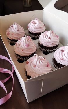 six cupcakes with pink frosting in a white box on a wooden table