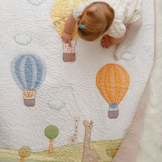 a baby is looking down at a blanket with hot air balloons on it