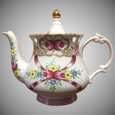 a white tea pot with flowers painted on the side and gold trimming around the top