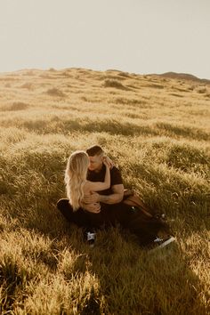 a man and woman sitting on the ground in an open field with their arms around each other