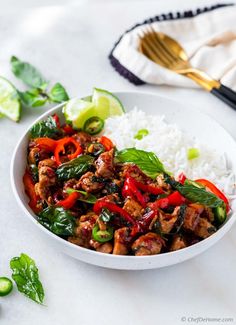 a white bowl filled with meat and vegetables on top of rice next to a fork