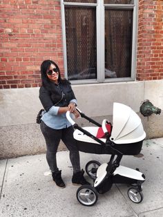 a woman standing next to a baby stroller on the side of a street with a brick building in the background