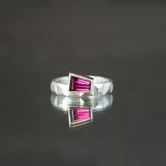 This listing is a for a one of a kind neon pink tourmaline and sterling silver ring, size 7, inspired by Jazz Age architectural design.  A fruity punch of pink is the cherry on top of this stackable statement ring. A tapered baguette of natural pink tourmaline is inset asymmetrically into a band of paneled sterling silver flash. The gem weighs 0.66 carat and exhibits a playful magenta-to-red color with heaps of neon flash. Its keystone shape melds perfectly with the Art Deco geometry of the patterned band. Bold enough to wear solo or add as a bookend to an existing ring stack - it is a size 7. This ring is one of kind and available to ship with 3 business days. Modern Red Ruby Ring, Modern Sterling Silver Ruby Ring, Modern Pink Gemstone Rings, Modern Ruby Open Ring Gift, Modern Ruby Open Ring For Gift, Modern Ruby Open Ring As Gift, Modern Open Ruby Ring As Gift, Modern Pink Ruby Ring For Gift, Modern Pink Ruby Ring As A Gift