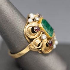 This knockout of a ring bring back visions of Renaissance jewelry- rich in colors and intricate in design. The ring features a center emerald cut emerald which is bezel set. The emerald has a closed back so we can't calculate the weight precisely, however it measures 10mm x 8.5mm, roughly calculating to 3.00ct. The stone is framed by four diamonds that measures 2.5mm each, totaling 0.24cttw. 2.8mm garnets accent the corners and the center top and bottom are highlighted by three seed pearls each. Fine Jewelry Emerald Ring With Intricate Design, Emerald Ring With Intricate Design, Heirloom Emerald Ring With Gemstone Accents For Formal Events, Victorian Emerald Jewelry In Emerald Cut, Victorian Emerald Jewelry With Emerald Cut, Victorian Style Emerald Cut Emerald Ring For Formal Occasions, Victorian Emerald Cut Emerald Jewelry, Multi-stone Emerald Cut Emerald Ring For May Birthstone, Emerald Cut Multi-stone Emerald Jewelry