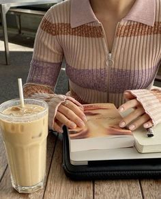 a woman sitting at a table with a book and a drink in front of her