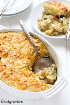 a casserole dish with chicken and cheese in it on a white table next to two silver spoons