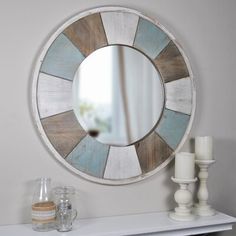 a round mirror sitting on top of a white dresser next to candles and vases