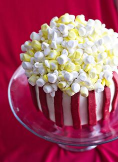 a red velvet cake with white and yellow candy toppings on top, sitting on a glass plate