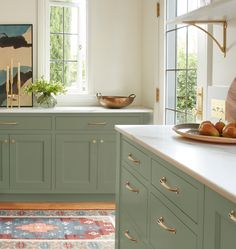 a kitchen with green cabinets and gold pulls on the handles, along with an area rug