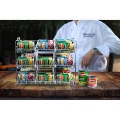 a man standing behind a stack of canned food on top of a wooden cutting board