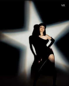 a woman in a black dress and hat posing for the camera with her hands on her hips