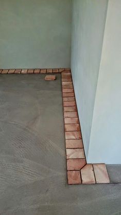 the corner of a room with a cement floor and brick edgings on it