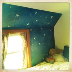 a bedroom with blue walls and white stars painted on the wall, along with a window